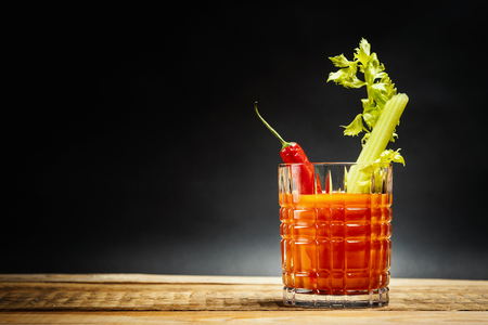 juicy red drink bloody mary with a piece of green celery and chilli peppers on a wooden tableの写真素材