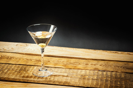 delicious martini drink with olive in a glass on a wooden tableの写真素材