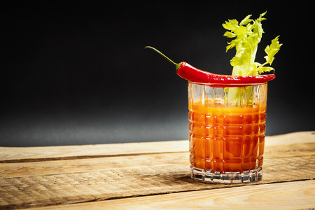 juicy red drink bloody mary with a piece of green celery and chilli peppers on a wooden tableの写真素材