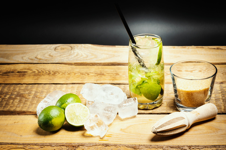 glass of delicious mojito on a wooden table with pieces of lime, ice and brown sugar on a black backgroundの写真素材
