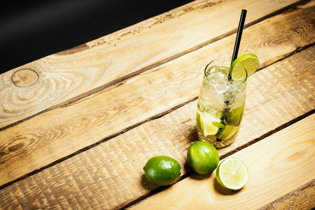 glass of delicious mojito on a wooden table with pieces of lime and mint leaves on a black backgroundの写真素材