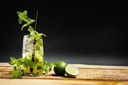 glass of delicious mojito on a wooden table with pieces of lime and mint leaves on a black backgroundの写真素材
