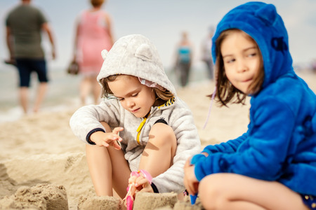 two little girls play with dolls in a sand castle on the beach in summerの写真素材