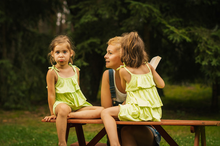 beautiful mother and two adorable daughters in dresses posing on a picnic table in a summer forestの写真素材