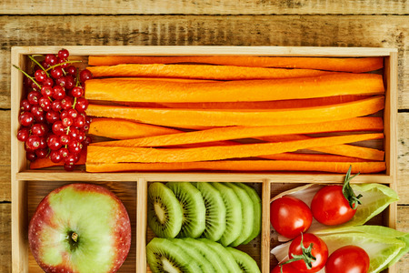 box with delicious carrots, apple, kiwi, cherry tomatoes and redcurrant on a wooden table