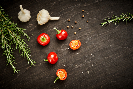 fresh and spicy red peppers, garlic and rosemary on a black wooden tableの写真素材