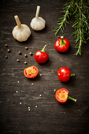 fresh and spicy red peppers, garlic and rosemary on a black wooden tableの写真素材