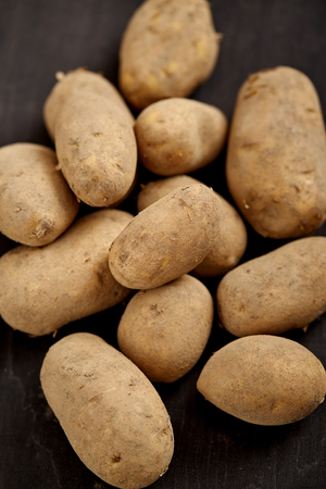 lots of young and fresh potatoes on a black wooden table in the kitchenの写真素材