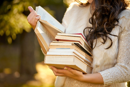 woman in a white sweater holding a pile of books against the backdrop of an autumn forestの写真素材