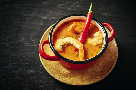 traditional Thai soup with shrimp and coconut milk in a red pot with chilli pepperの写真素材