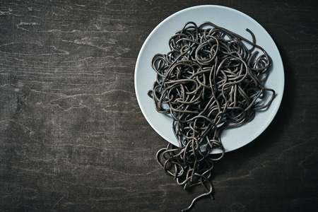 cooked black spaghetti pasta on a gray plate on a black wooden tableの写真素材