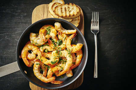 fresh delicious fried tiger prawns in a pan and toasts on wooden boardの写真素材