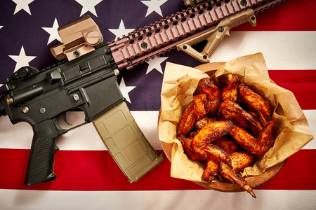 top view of delicious fried chicken wings and machine gun against USA flag backgroundの写真素材