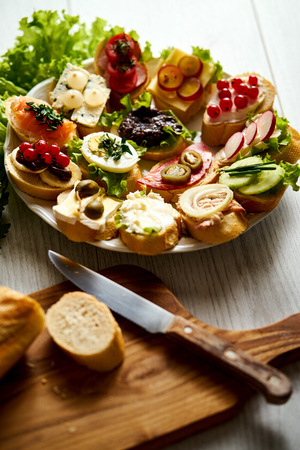 plate of colorful and healthy sandwiches or tapas with a knife and a baguette on wooden tableの写真素材