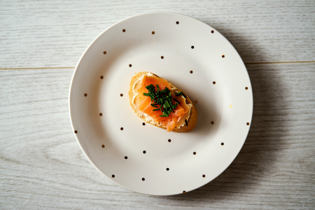 plate with a mini sandwich or tapas with salmon cheese and chives on a wooden tableの写真素材