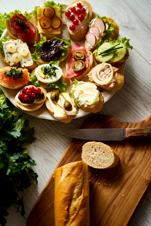 plate of colorful and healthy sandwiches or tapas with a knife and a baguette on wooden tableの写真素材