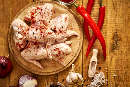 Fresh organic chicken wings on a chopping board with spices and vegetables on wooden table.の写真素材