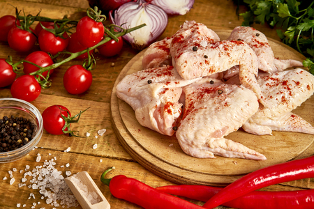 Fresh organic chicken wings on a chopping board with spices and vegetables on wooden table.の写真素材