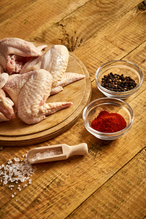 Fresh organic chicken wings on chopping board with chili pepper and salt on wooden table.の写真素材