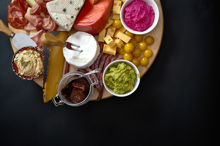 Antipasti board with various cheese and meat snacks with hummus and olives on wooden round board