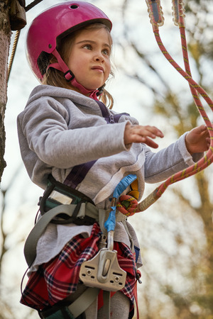 Adorable little girl in helmet in rope park in forestの写真素材
