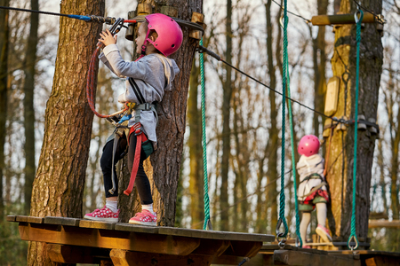 Two adorable little girls in helmet in a rope park in the woodsの写真素材