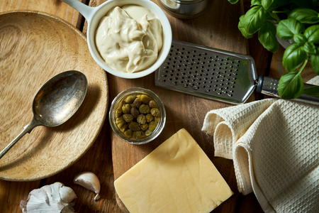 Cheese and grater fresh basil with can and sauce on wooden kitchen tableの写真素材