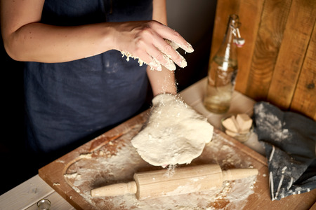 Woman prepares dough on pastry board with flour and rolling pin on white wooden tableの写真素材