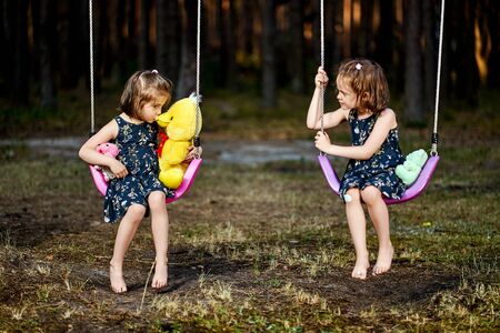 Two cute little girls on swing in forest on summer day