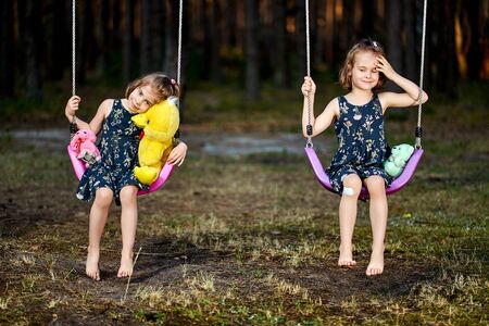 Two cute little girls on swing in forest on summer dayの写真素材