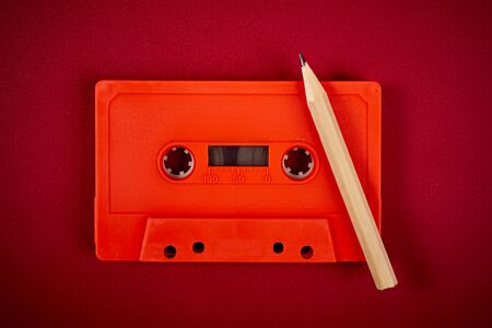 old orange audio cassette and pencil on dark red backgroundの写真素材