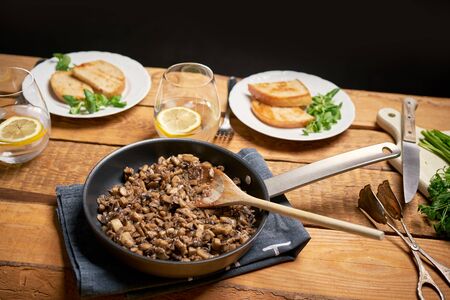 Stewed mushrooms in pan with toasts and parsley on wooden tableの写真素材