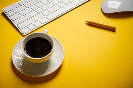 Top view of white keyboard and cup of coffee on yellow deskの写真素材