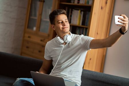 Handsome man sitting on sofa with laptop and taking selfie.の写真素材