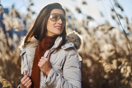 Beautiful woman in jacket poses on meadow on sunny dayの写真素材