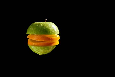 Sliced apple and orange with water droplets on black backgroundの写真素材