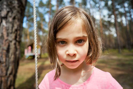 adorable little girl sits on a swing and makes facesの写真素材