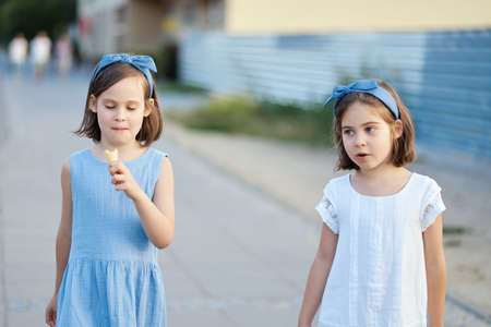 two cute little girls walk around the city and eat ice creamの写真素材