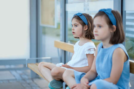 two little girls sit on the bench waiting for the busの写真素材