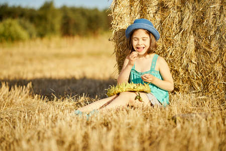 adorable girl eating sunflower seeds on mown rye in the fieldの写真素材