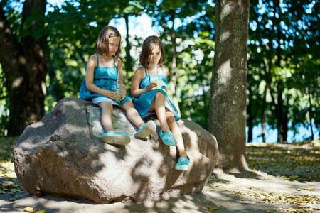 two cute little girls in dresses sit on a stone and drink lemonadeの写真素材