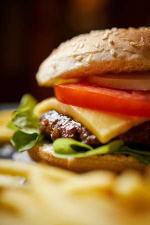 delicious cheeseburger surrounded by french fries on a black tableの写真素材