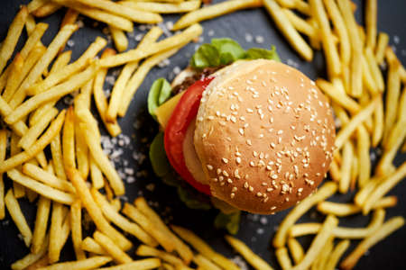 delicious cheeseburger surrounded by french fries on a black tableの写真素材
