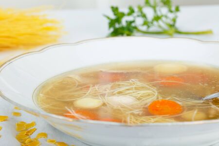 Chicken soup with noodles and vegetables in white plateの写真素材