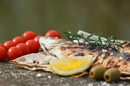 Grilled fish served on a paper with tomato,m onion and olives and decorated with rosemary and lemonの写真素材