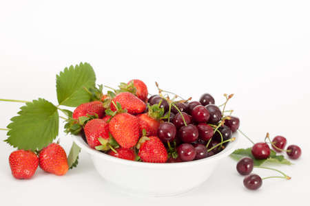 White bowl with fresh strawberries and cherries, white background. Healthy fruit.の写真素材