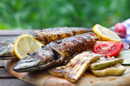 Grilled mackerel fish with lemon and vegetables on wooden board.の写真素材