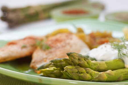 Roasted chicken breast meat and asparagus with sauce on green plate. Asparagus meal decorated with lemon and dill. Homemade cuisine. Close up image, shallow depth of field.の写真素材