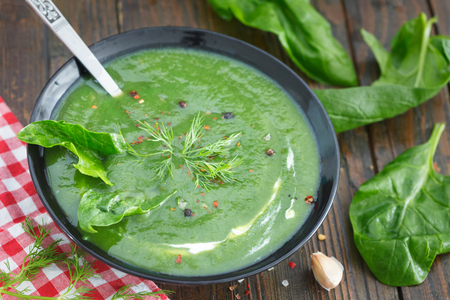 Green spring pureed spinach soup in a bowl decorated with dill. Salt, pepper, garlic and leaves of fresh spinach on wooden tableの写真素材