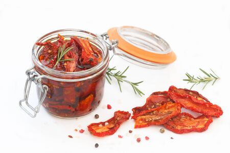 Sun dried tomatoes with herbs and spices in glass jar on white background. Healthy food ingedients for delicous cooking. の写真素材